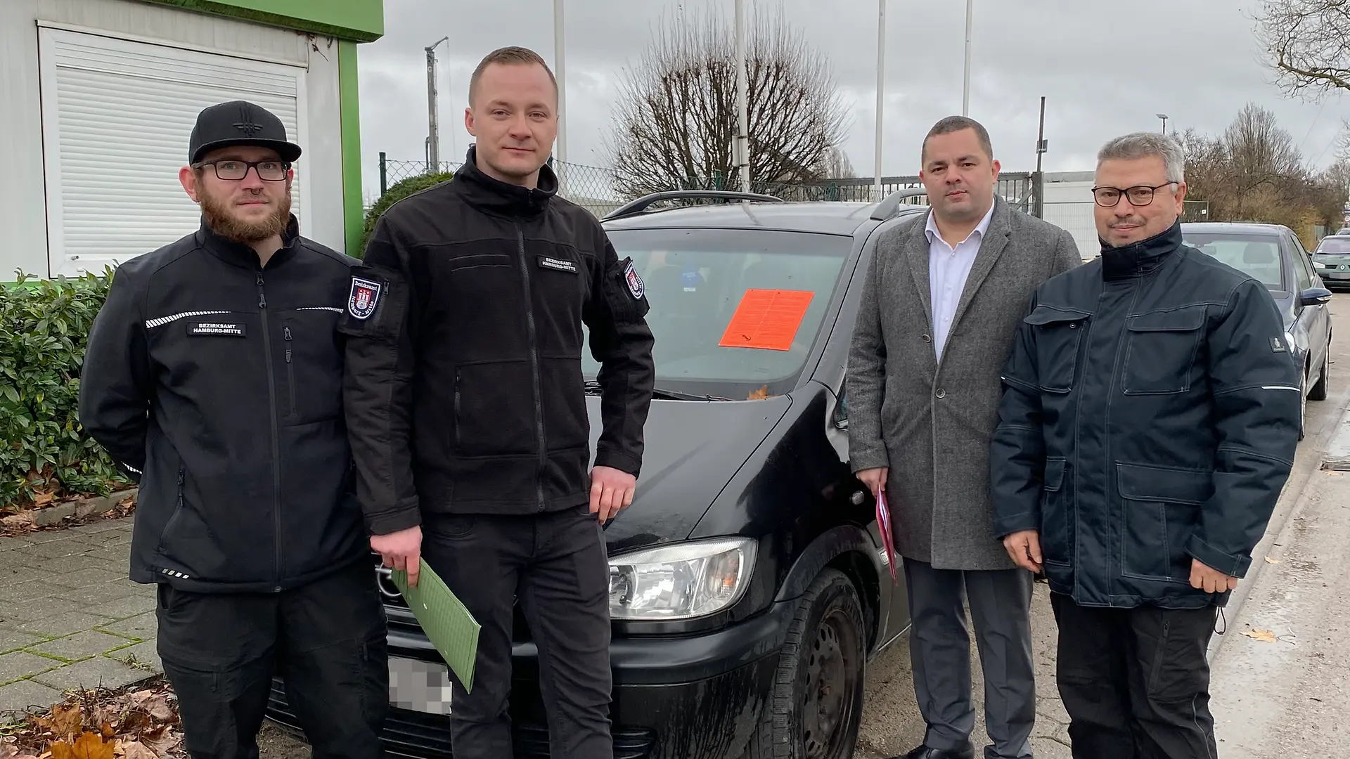 Vier männliche Personen stehen vor einem einem Personenkraftwagen.