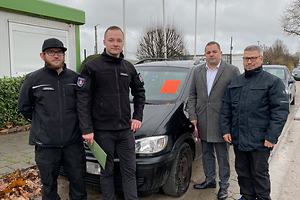 Vier männliche Personen stehen vor einem einem Personenkraftwagen.