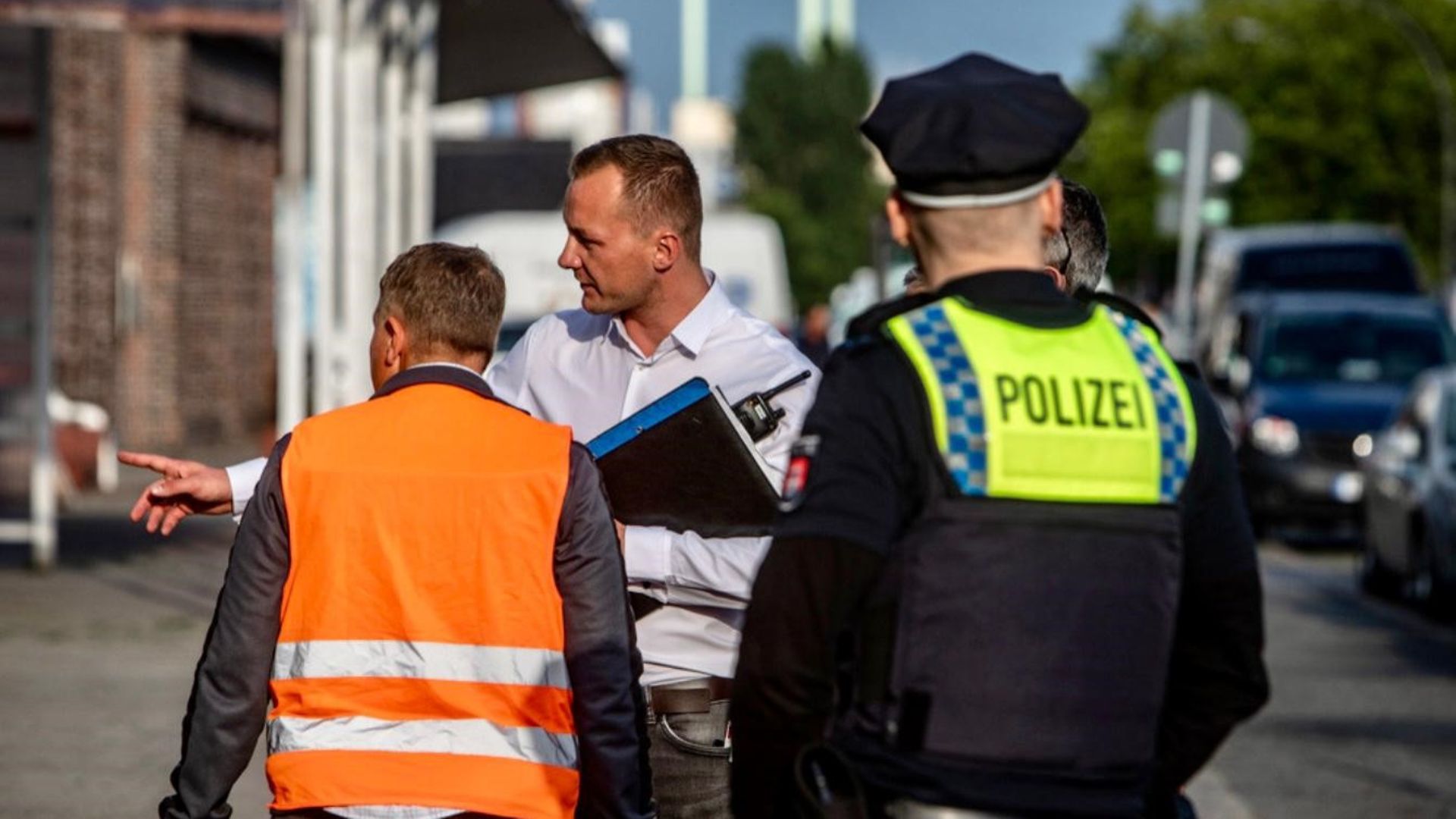 Mehrere Polizisten unterwegs auf der Straße. Ein Beamter weist eine Person in eine Richtung. 
