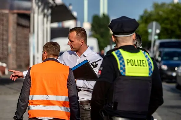 Mehrere Polizisten unterwegs auf der Straße. Ein Beamter weist eine Person in eine Richtung. 